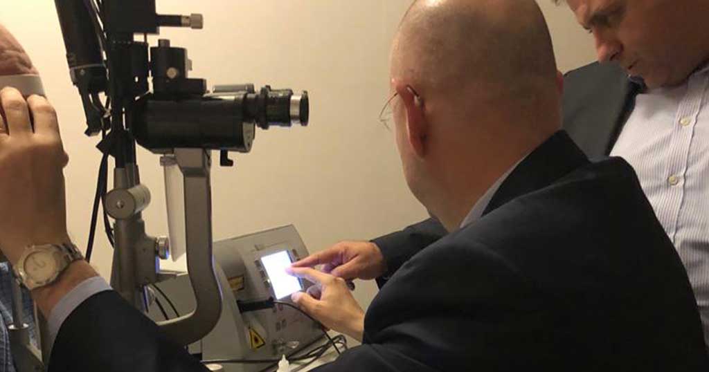 Two eye doctors in suits examining and adjusting settings on an ophthalmic device with a touchscreen, likely preparing or demonstrating an eye examination.