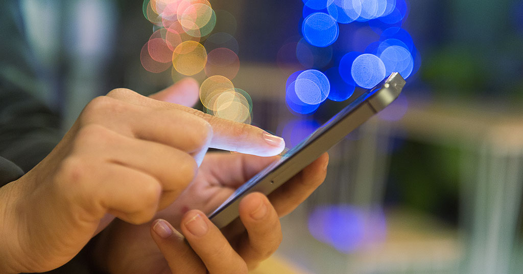 Close-up of a person using a smartphone with bright blue light and bokeh in the background, highlighting blue light exposure risk.