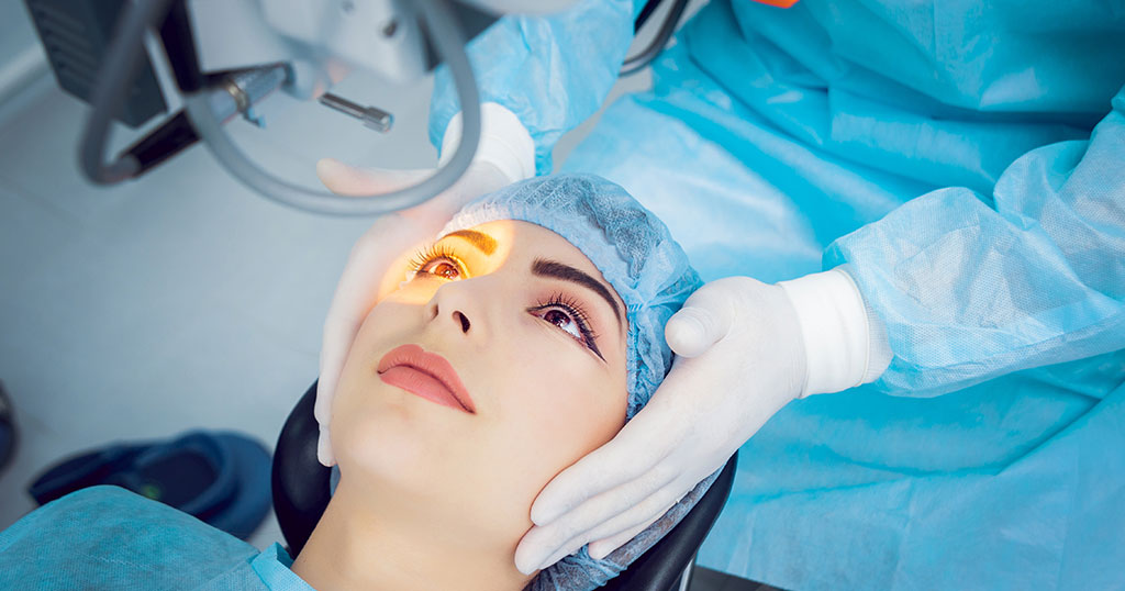 Patient undergoing laser eye surgery with a bright light focused on the eye, wearing a surgical cap and assisted by a medical professional in blue scrubs.