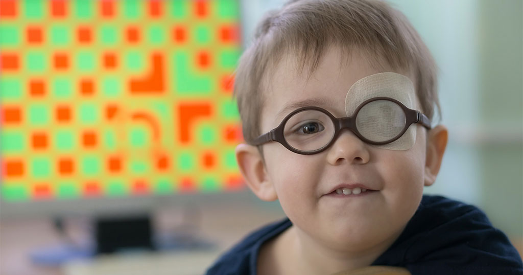Young boy wearing glasses with a patch over one eye, likely undergoing treatment for amblyopia (lazy eye), with a colorful vision therapy screen in the background.