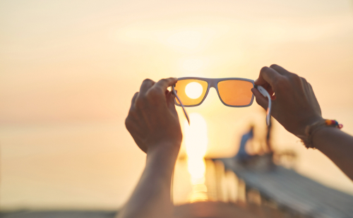 Hands holding sunglasses against a sunset, illustrating UV eye protection.
