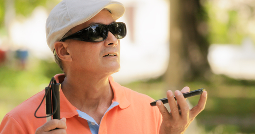 Blind man using assistive smartphone technology outdoors, holding a folded cane.
