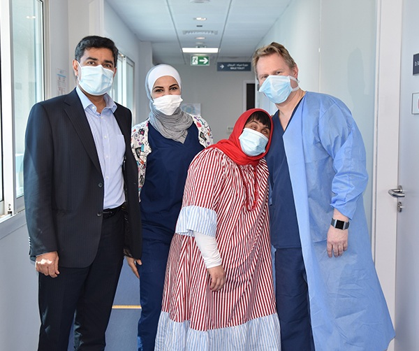 Four people wearing face masks, including ophthalmologists in Abu Dhabi, standing together in a hospital corridor with a patient.