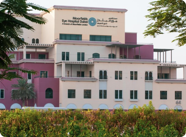 Exterior view of Moorfields Eye Hospital Dubai building in Dubai Healthcare City with cream and purple facade surrounded by trees and greenery