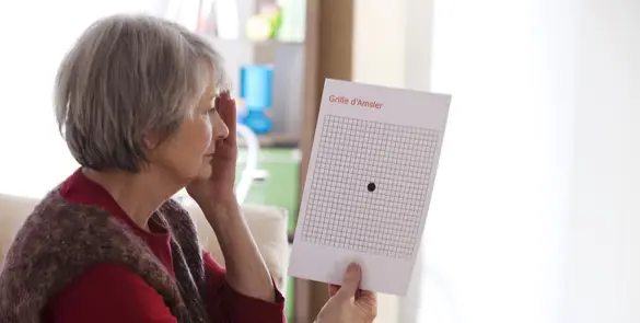 Older woman using an Amsler grid at home to monitor central vision changes linked to macular conditions.